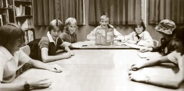 A black and white picture of seven youths sitting around a large table playing Dungeons and Dragons in the 1980s