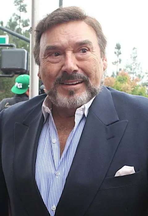A mature gent with brown hair and eyes and a salt and pepper trimmed beard stands in a dark blue suit and smiles while looking off to the right.