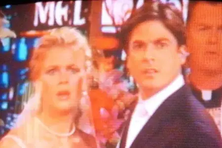 On a television screen is a wedding scene, but the blond bride and dark haired groom are looking off-screen in shock.