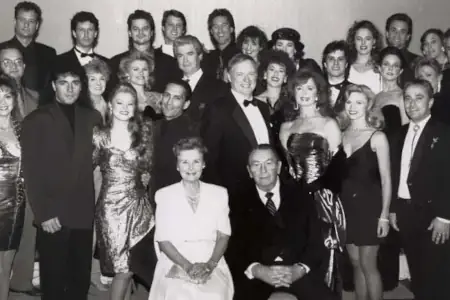 In this black and white photo, men in suits and women in dresses are arranged in rows